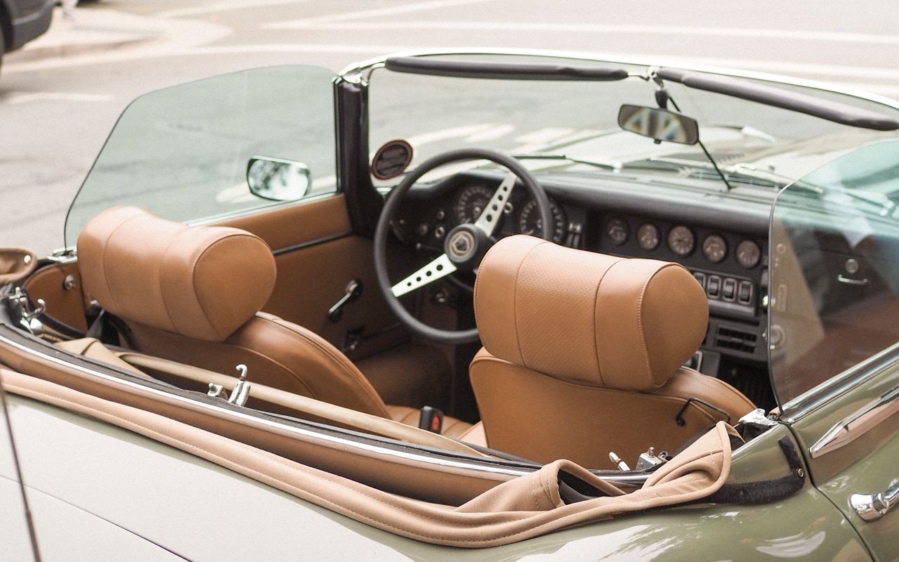 A classic Jaguar E-Type convertible with a tan leather interior and a green exterior