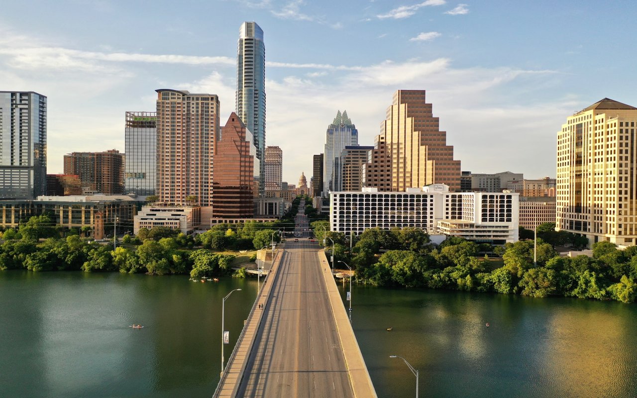 A wide bridge stretches across a river leading to a vibrant city skyline.