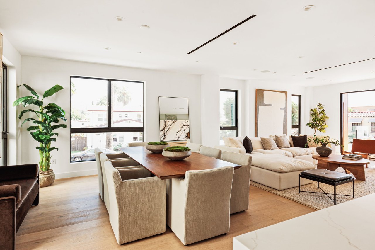 A bright and modern open-concept living space with a dining area in the foreground and a living room beyond.