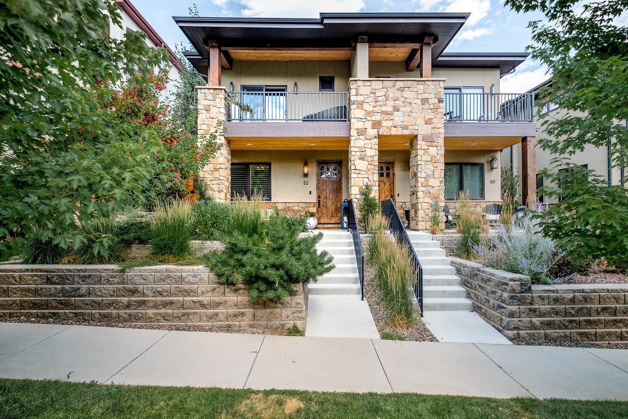 Two-story red brick home with gabled roof, green shingles, white picket fence, porch with brown door, double-hung windows, and walkway.