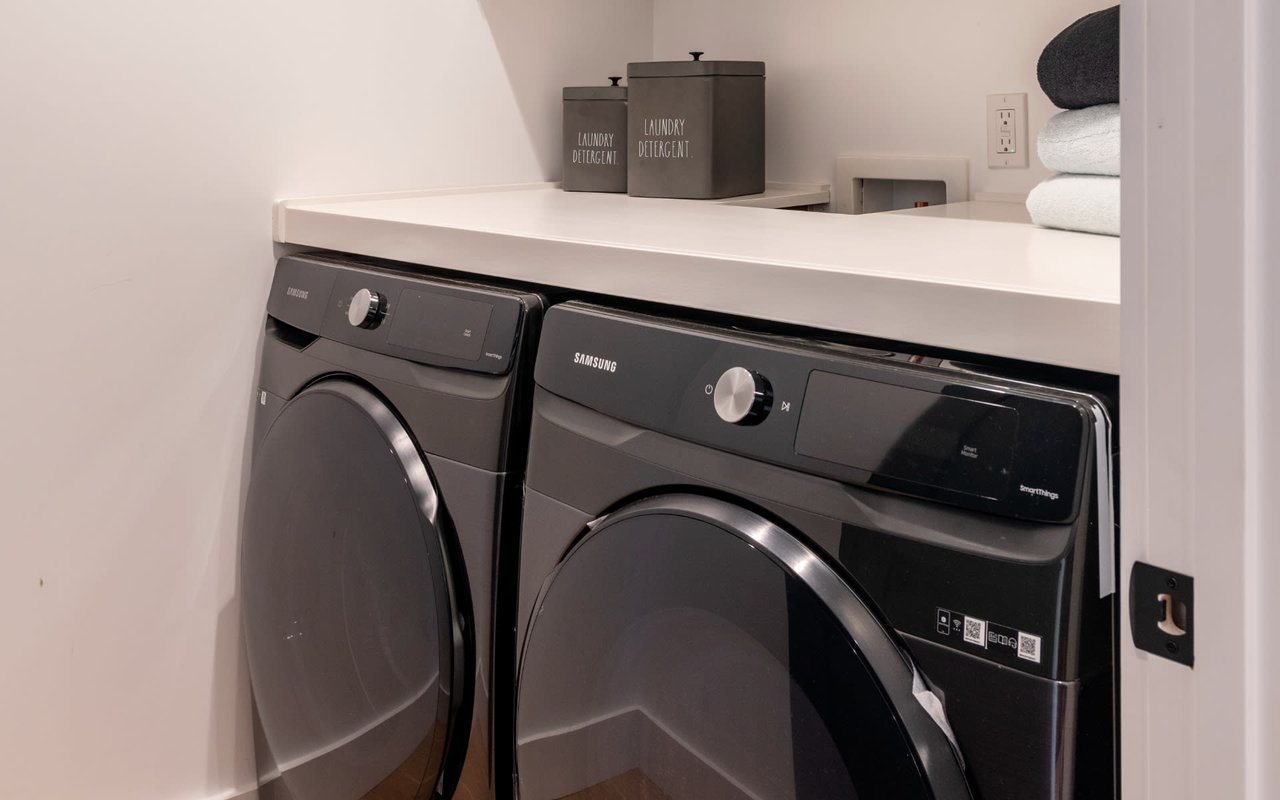 Laundry room with dark front-loading washer and dryer beneath a white countertop.