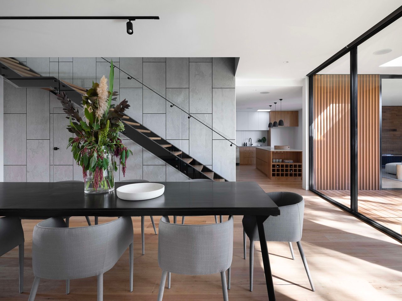 A modern staircase with a black railing and open risers is set against a textured grey wall.