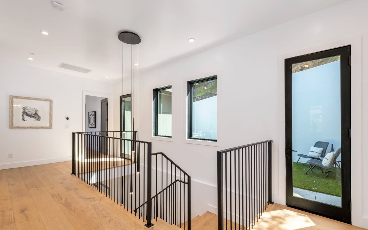 Upper hallway with light wood floors, black stair railings, and a tall glass door to the outdoors.