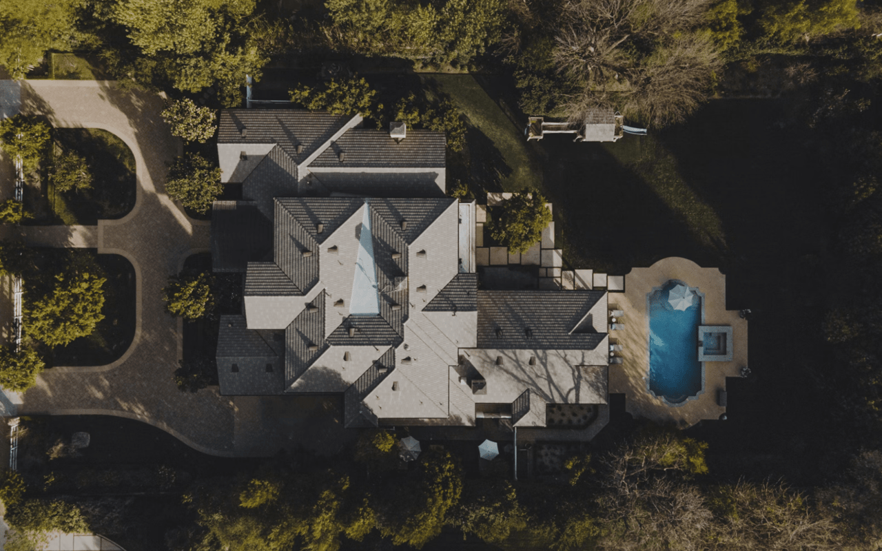  An aerial view captures a sprawling luxury estate, its complex roofline a mosaic of dark gray shingles and lighter sections.