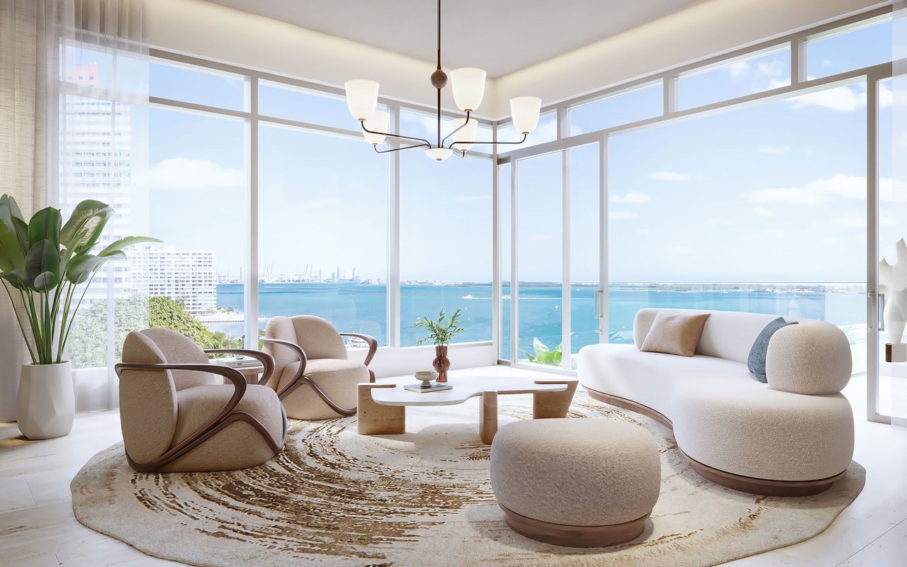 Furnished living room with floor-to-ceiling windows overlooking turquoise water.