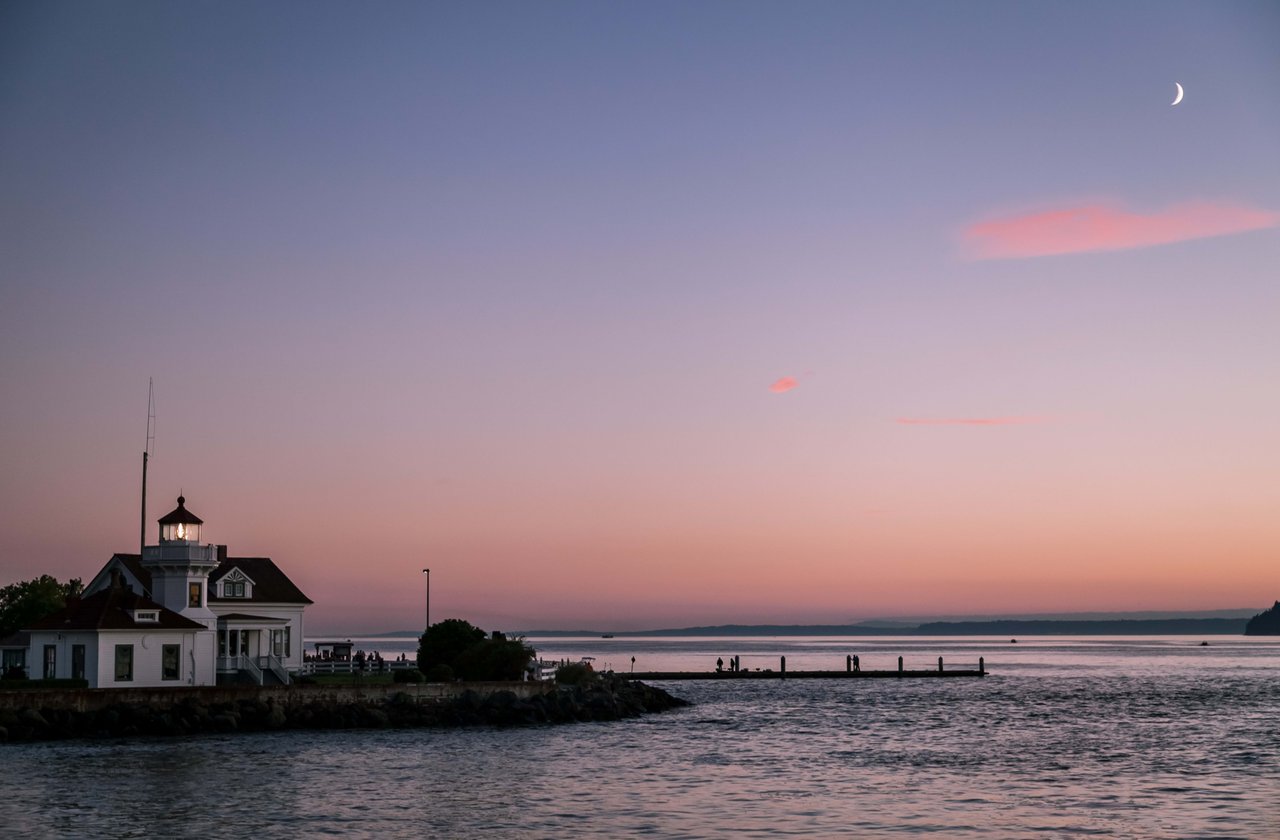 A white lighthouse stands on a rocky peninsula at twilight