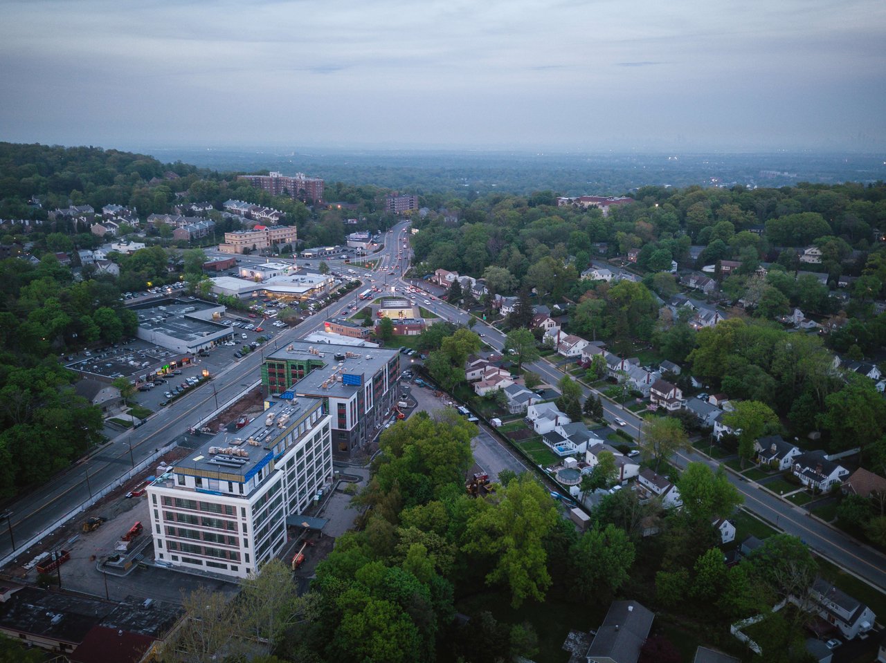 Aerial view of a busy intersection, surrounded by houses and trees, and a large brick building at the center.