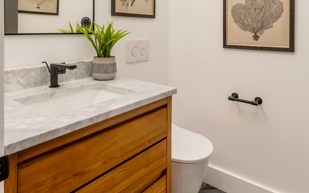 Modern bathroom with a wood vanity, marble counter, black faucet, and framed botanical prints.