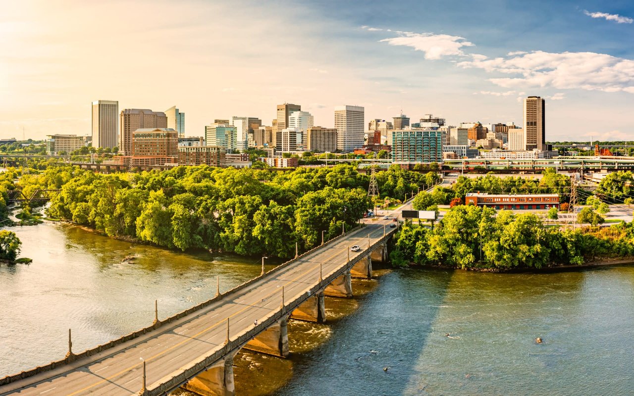 An aerial view captures a wide river with a long bridge spanning across it, leading to a vibrant city skyline