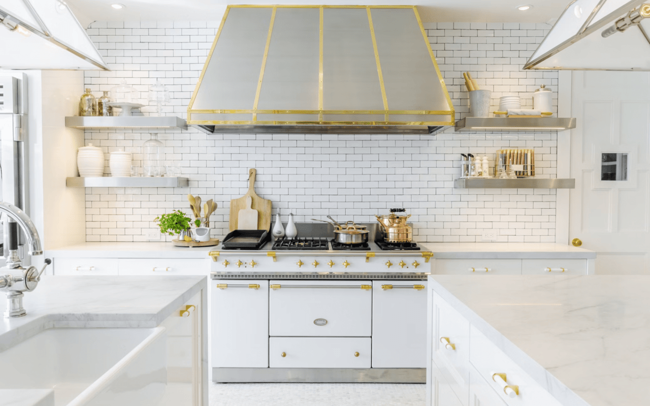  A spacious and elegant kitchen features a large white island with a light-colored countertop and intricate gold-colored handles on its many cabinets and drawers.