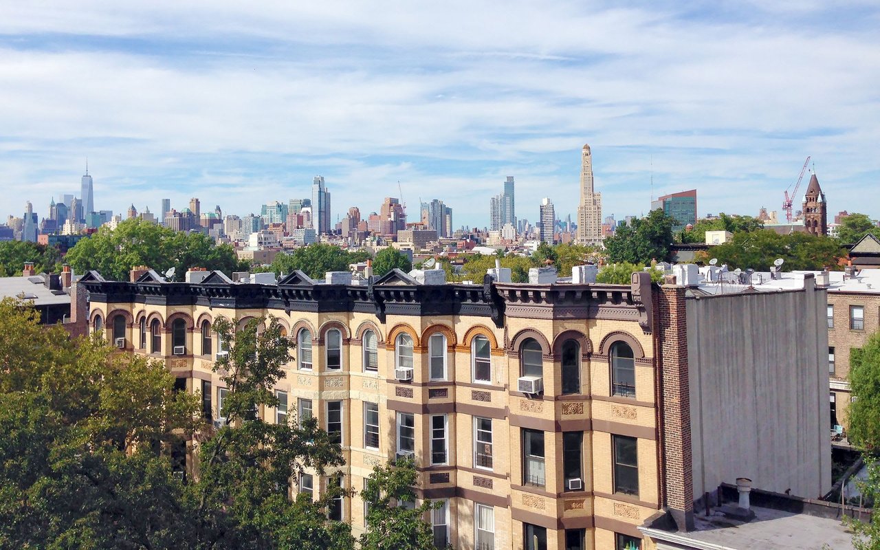 Row of brownstone apartments with fire escapes, New York City skyline in background.  pen_spark