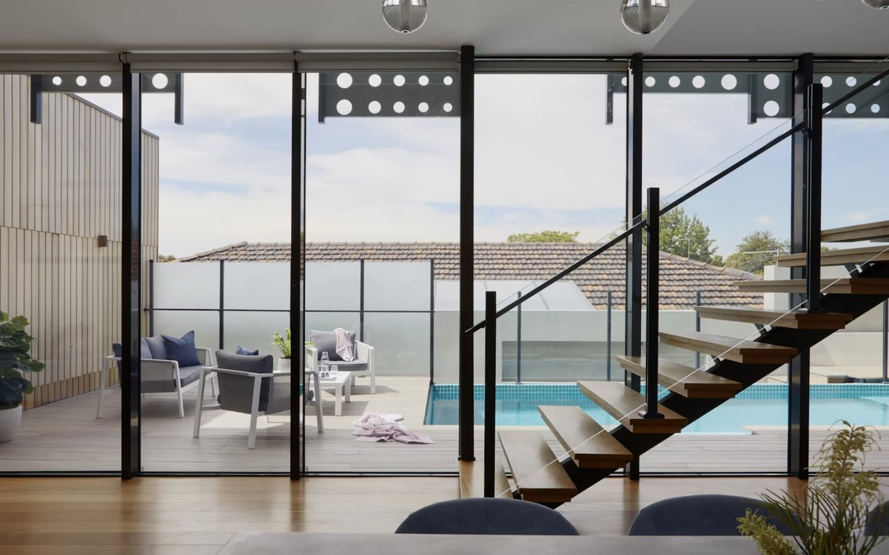  A modern indoor space with light wooden flooring opens to an outdoor deck and swimming pool 
