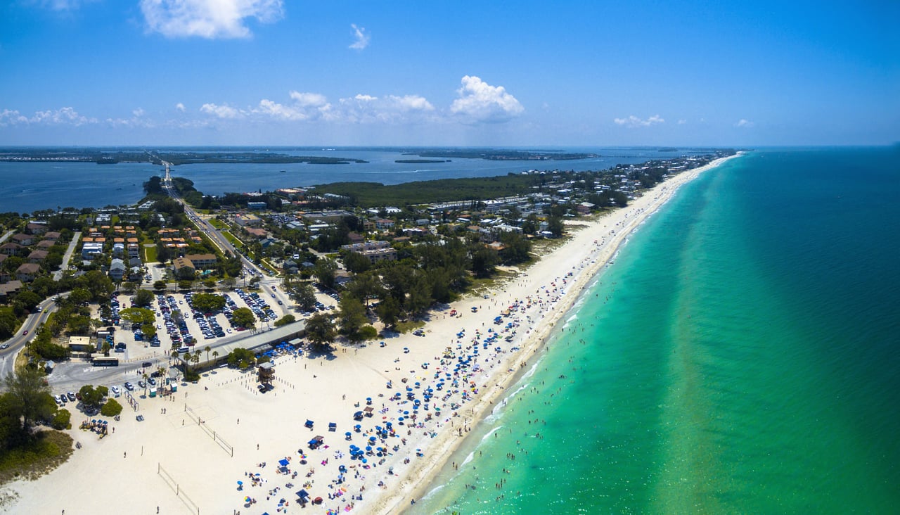 The clear turquoise ocean water stretches out to the right, while residential areas, roads, and a bridge connecting to the mainland are visible to the left.