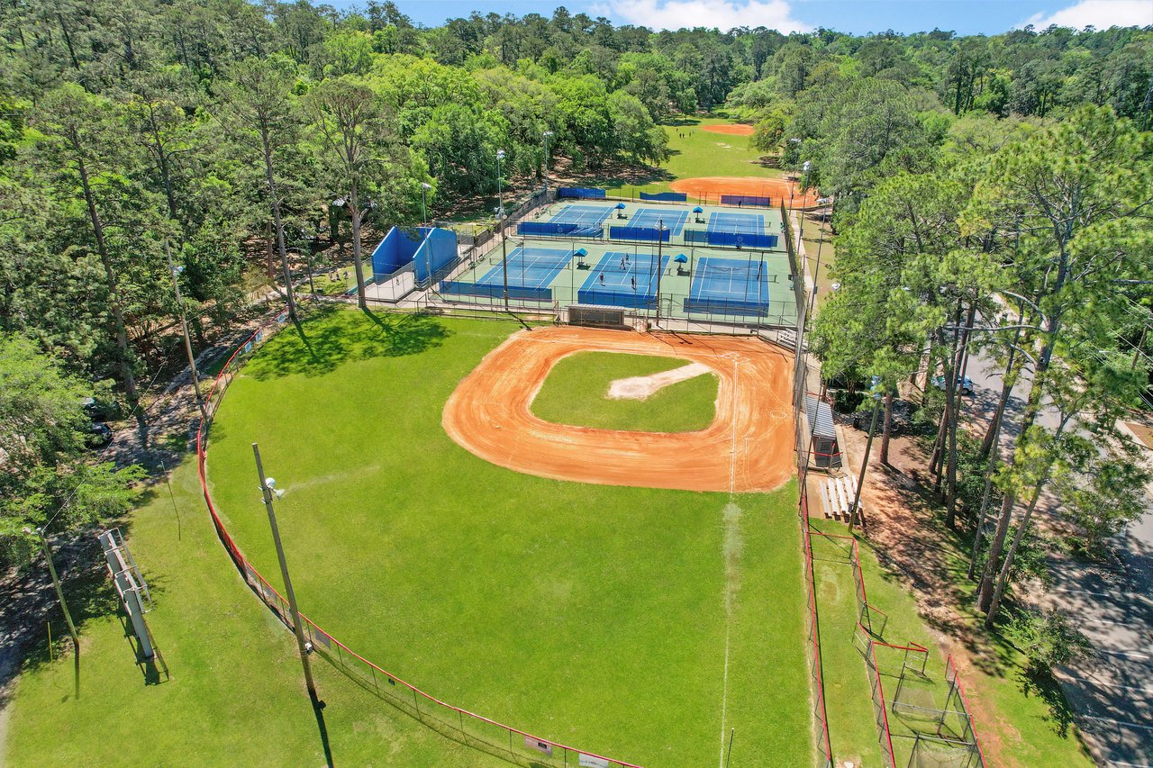 An aerial view of a recreational area in the Betton Hills neighborhood, featuring a baseball field and tennis courts surrounded by trees.