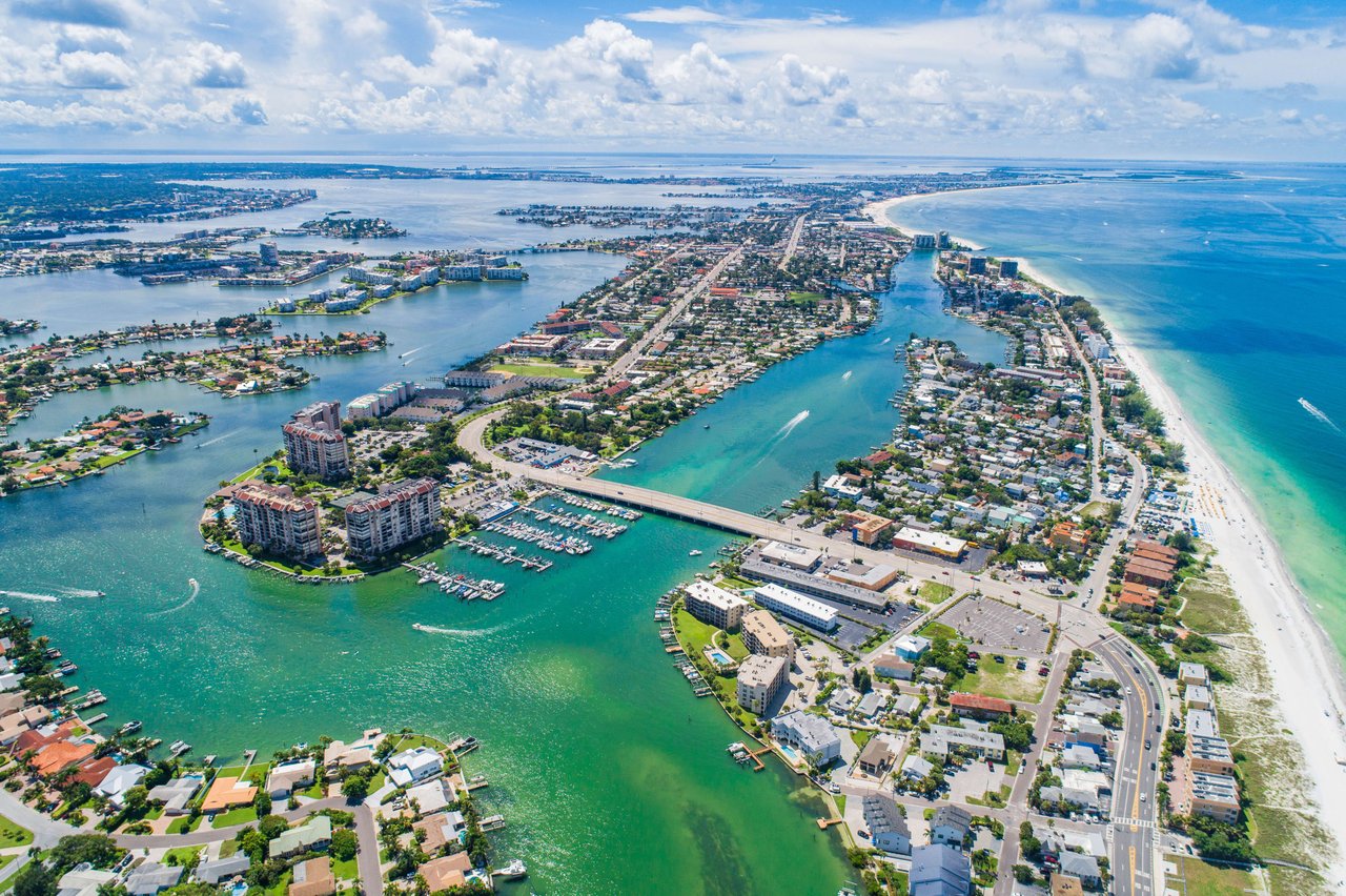 An expansive aerial view captures a vibrant coastal landscape under a bright, partly cloudy sky.