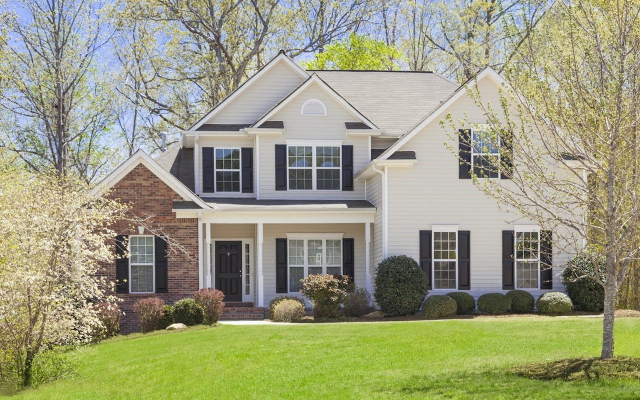  A charming suburban house with light yellow siding and dark brown shutters, featuring a mix of brick and siding on its exterior