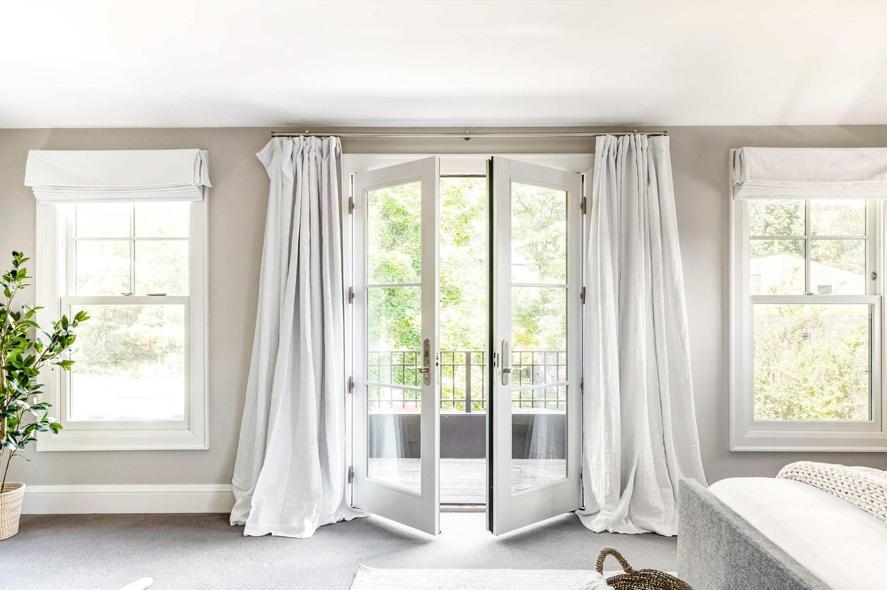 Bedroom with French doors, floor-length drapes, and natural light from multiple windows