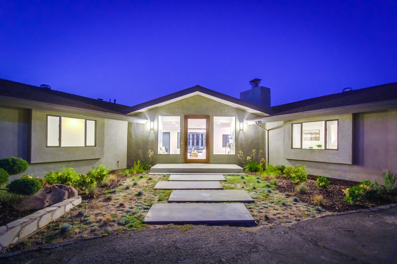 Modern home at night with a glass entry, illuminated windows, and stepping-stone path.
