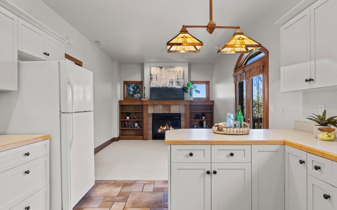 585 N Morningside Way's ADU. In front, white shaker kitchen cabinets with Arts & Crafts stained glass lights overhead. In back, a fireplace with built-ins and windows on either side.