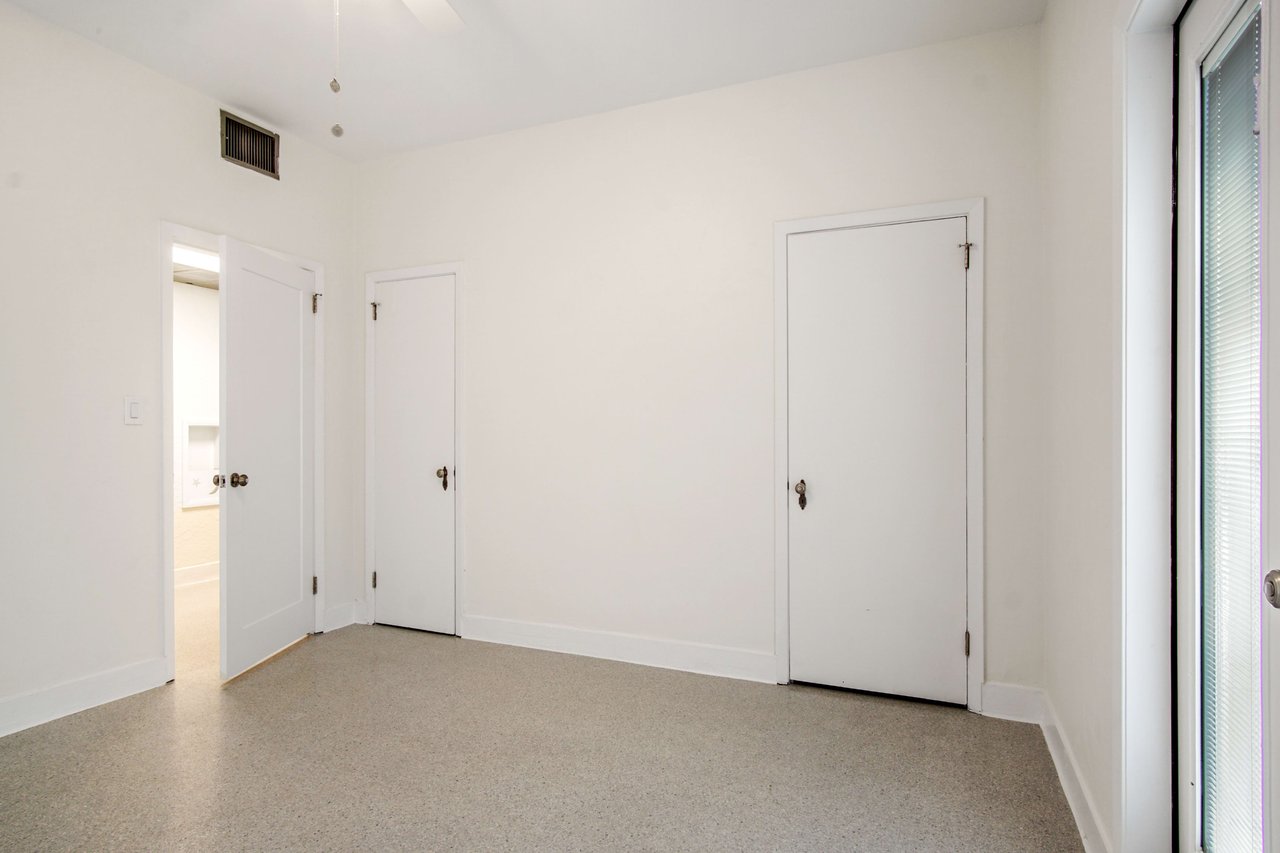 A  second bedroom with a closet and a window decorated with neutral colors.