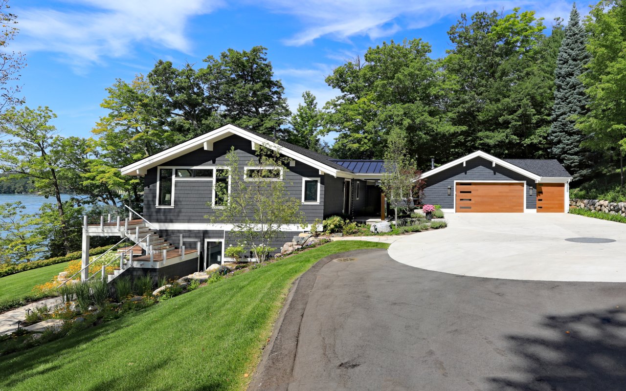  A modern dark grey house with white trim and a black roof is nestled among lush green trees