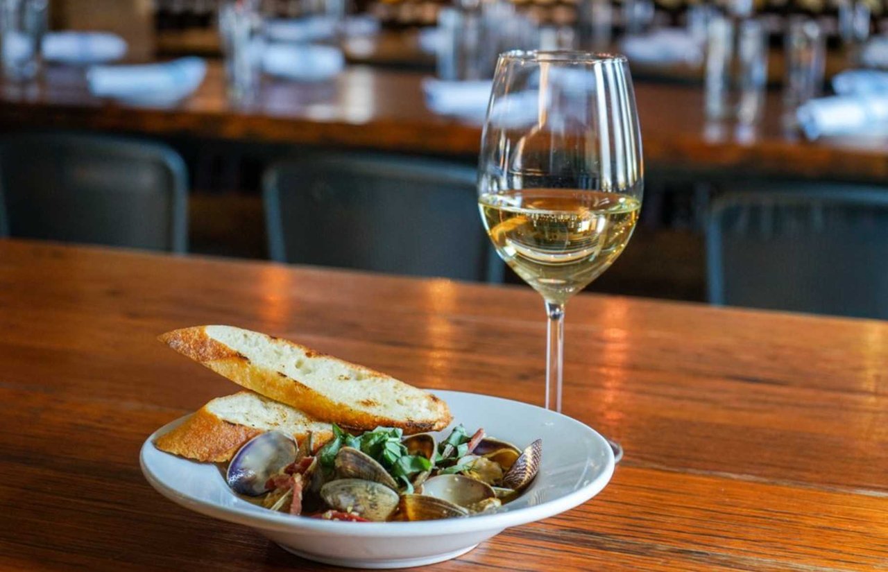 a photo of a bowl of steamed mussels next to a glass of white wine