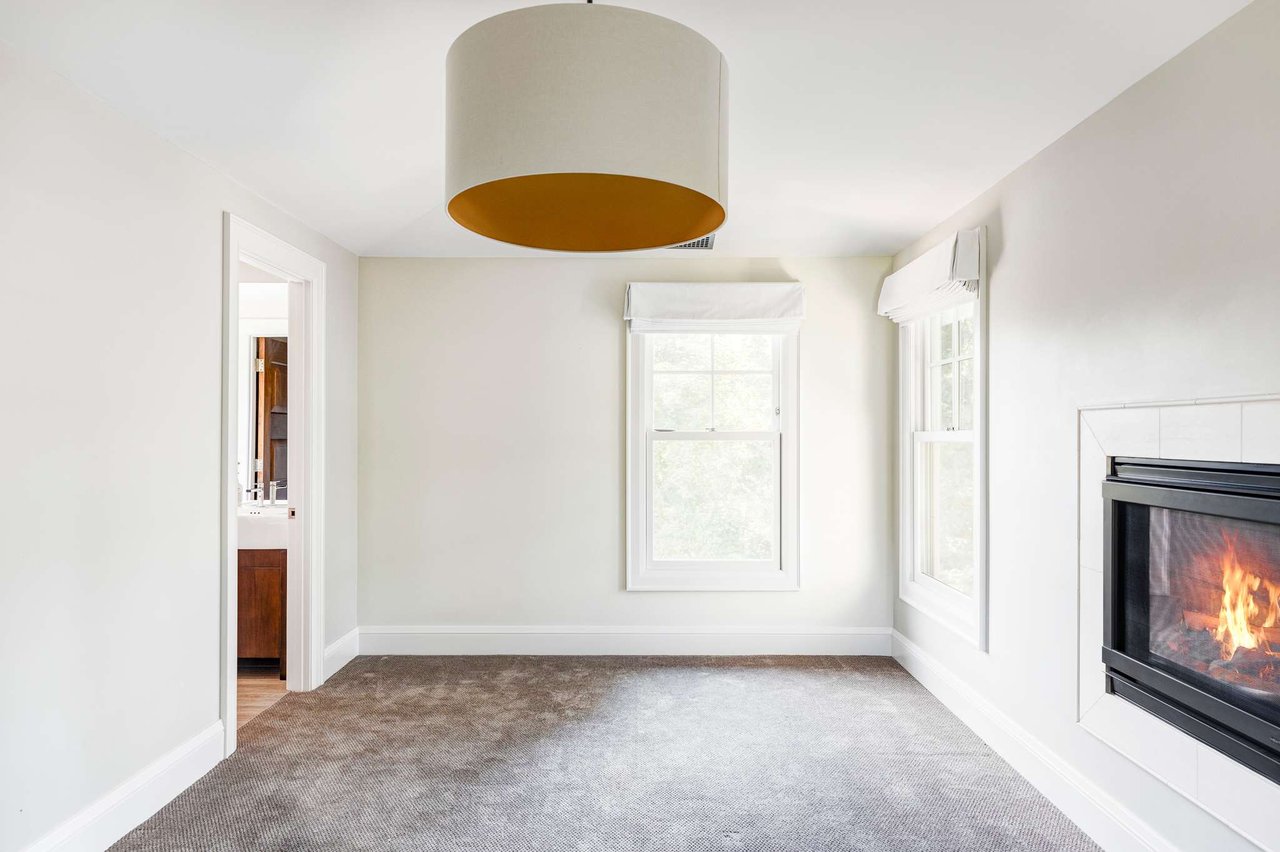 Empty guest bedroom with gas fireplace, drum pendant light, and doorway to bathroom