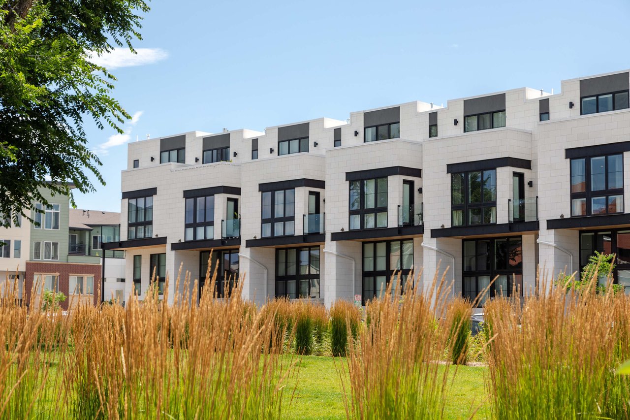 Row of white apartment buildings with balconies stand next to a field of tall green grass