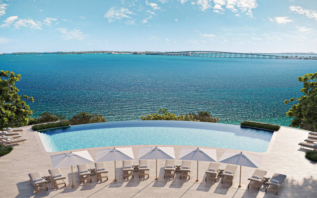 Curved waterfront pool deck with lounge chairs and umbrellas overlooking the bay.