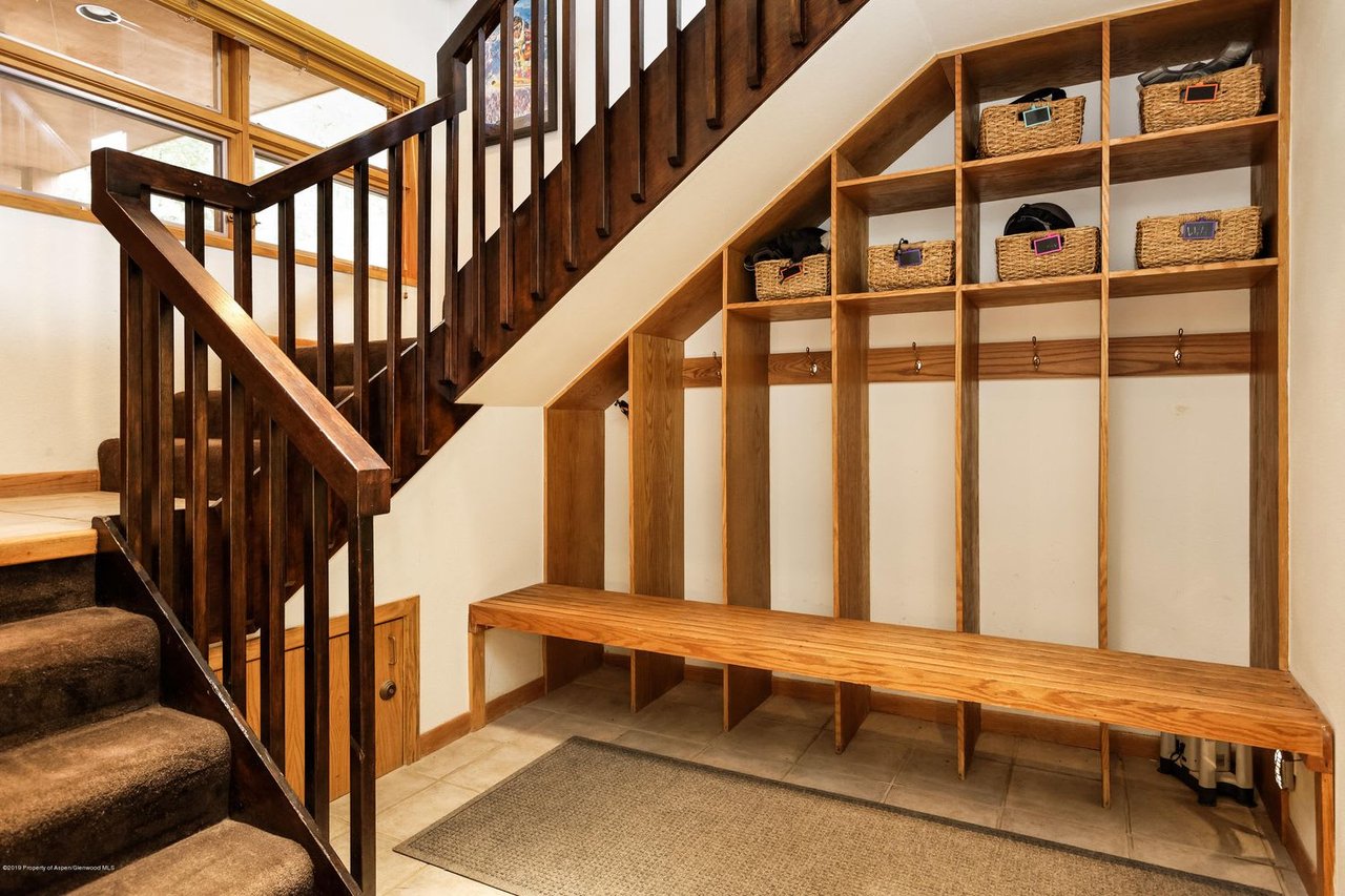 Mudroom with a dark wood staircase, built-in cubbies, wicker baskets, hooks, and a long wooden bench.
