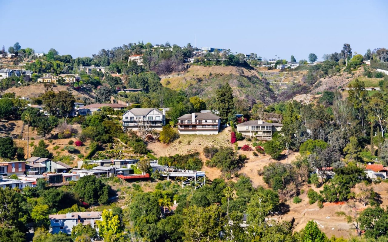 An expansive, high-angle view of a residential area built into rolling, verdant hills under a clear blue sky.