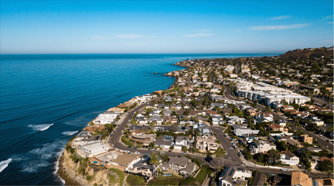 Aerial view of coastal homes along the Pacific shoreline, with cliffs and a hillside neighborhood.