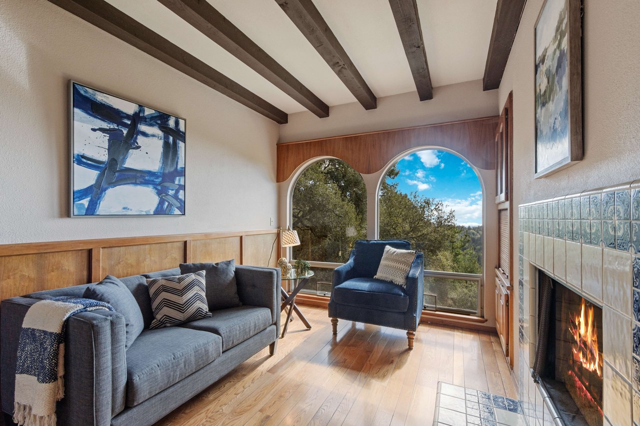 Living room with arched windows, exposed ceiling beams, and a tiled fireplace.