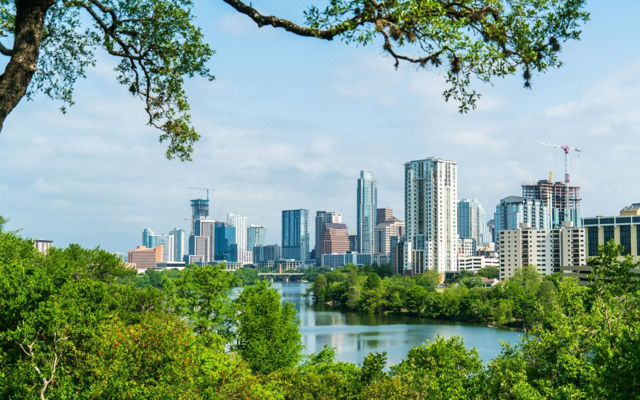 Vibrant cityscape framed by lush greenery, reflecting on a calm river.