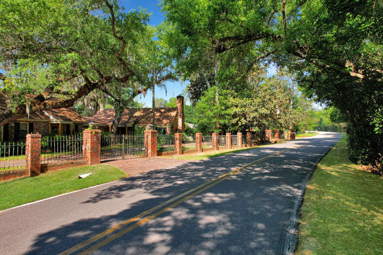 A ground-level view of a road in Lake Bradford with trees lining both sides. There is a fence along the road, and the area appears green and well-maintained.