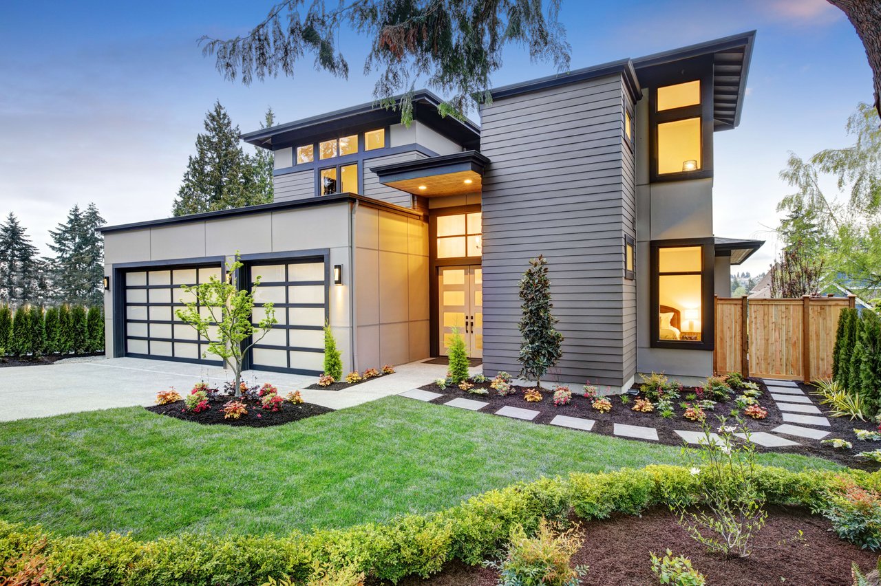 A modern house with a glass garage door and a lush green yard.