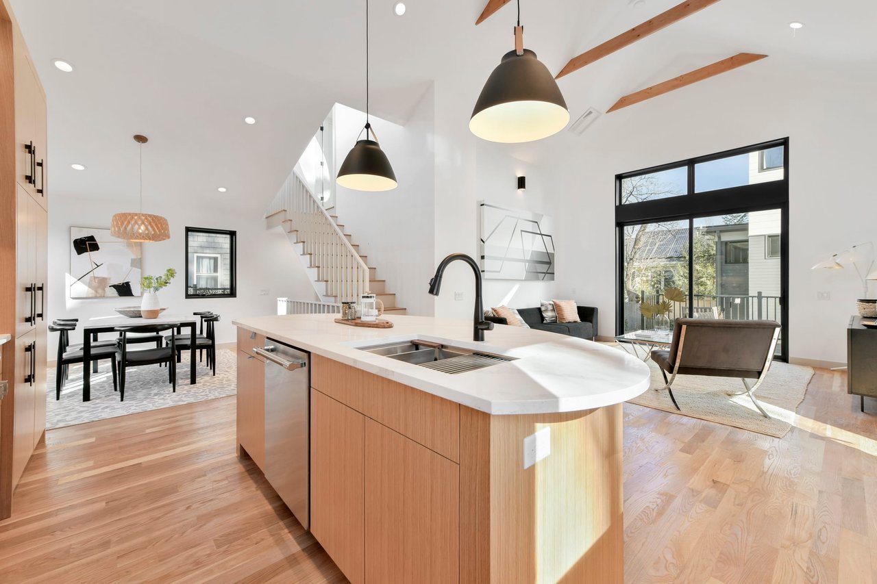 Modern kitchen with island, pendant lights, and wooden flooring, open to dining and living areas.