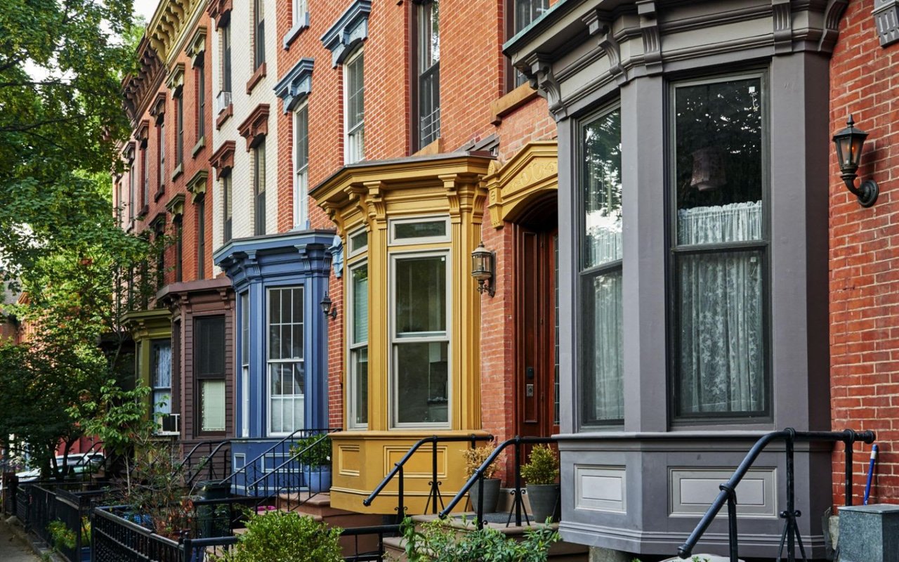  A street-level view of a row of historic brick townhouses with colorful bay windows and ornate details.