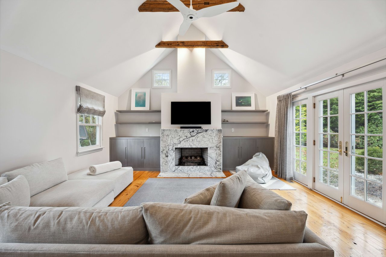 Minimalist living room with exposed beams, marble fireplace, and gray furniture.