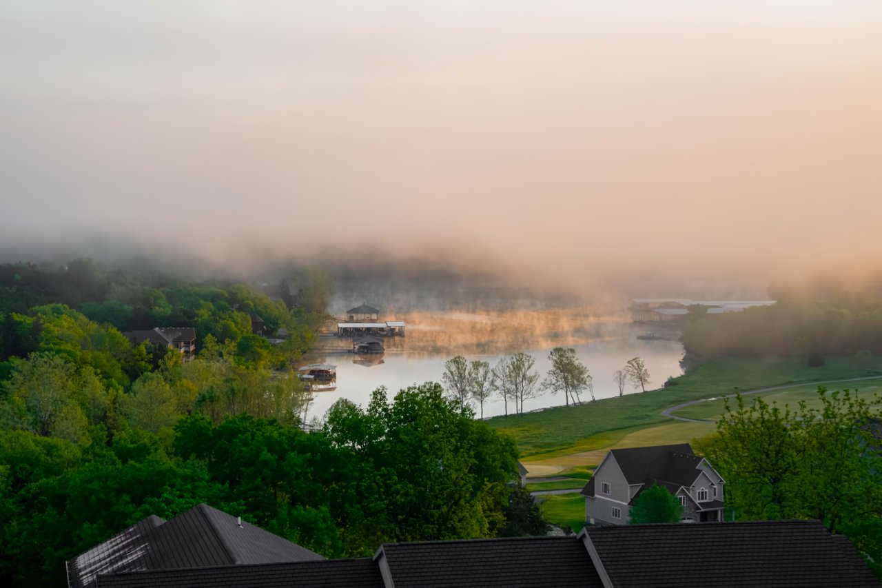  A serene, hazy morning scene overlooks a lake partially obscured by mist
