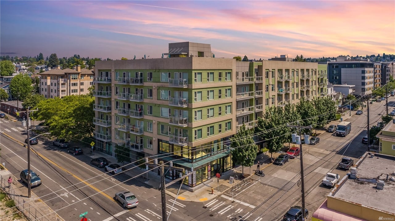 Corner view of a green modern condo building at dusk, blending urban lifestyle with vibrant skies.