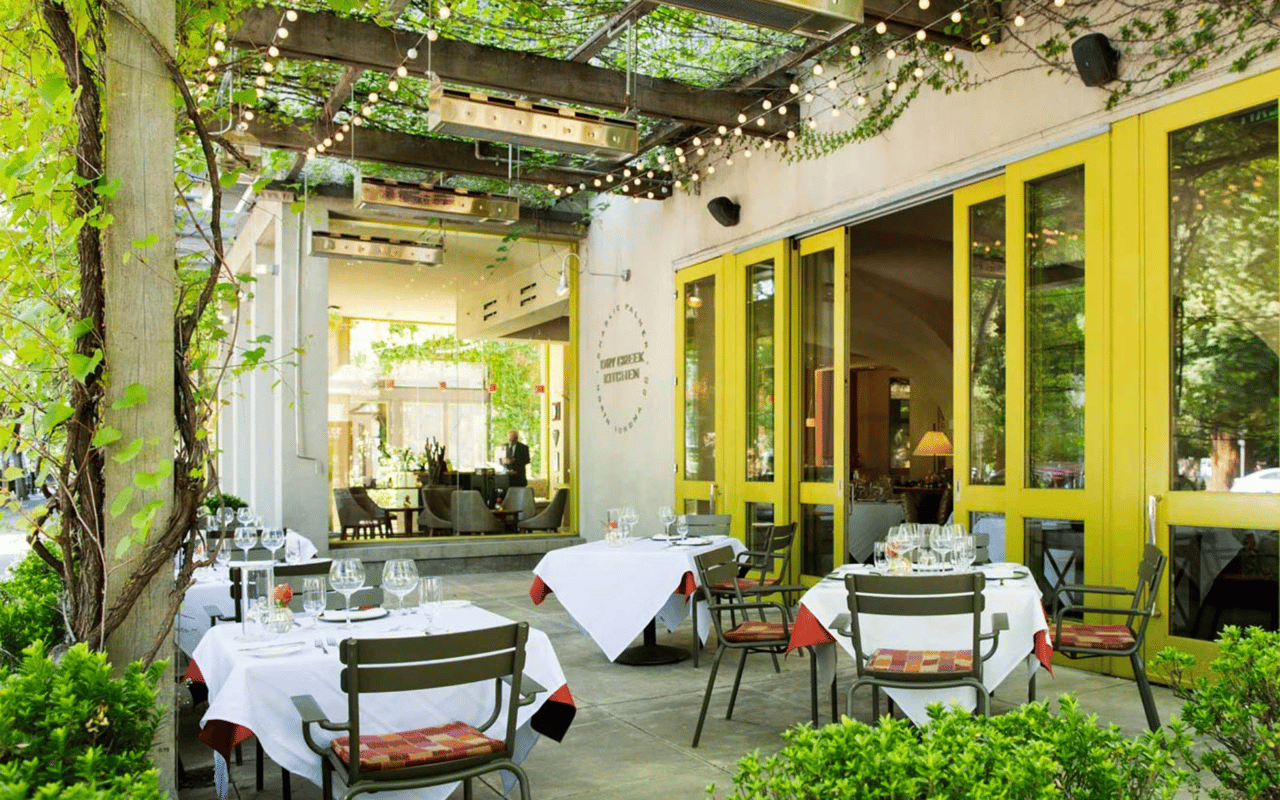 An outdoor dining patio with tables, chairs, and a wooden pergola roof.