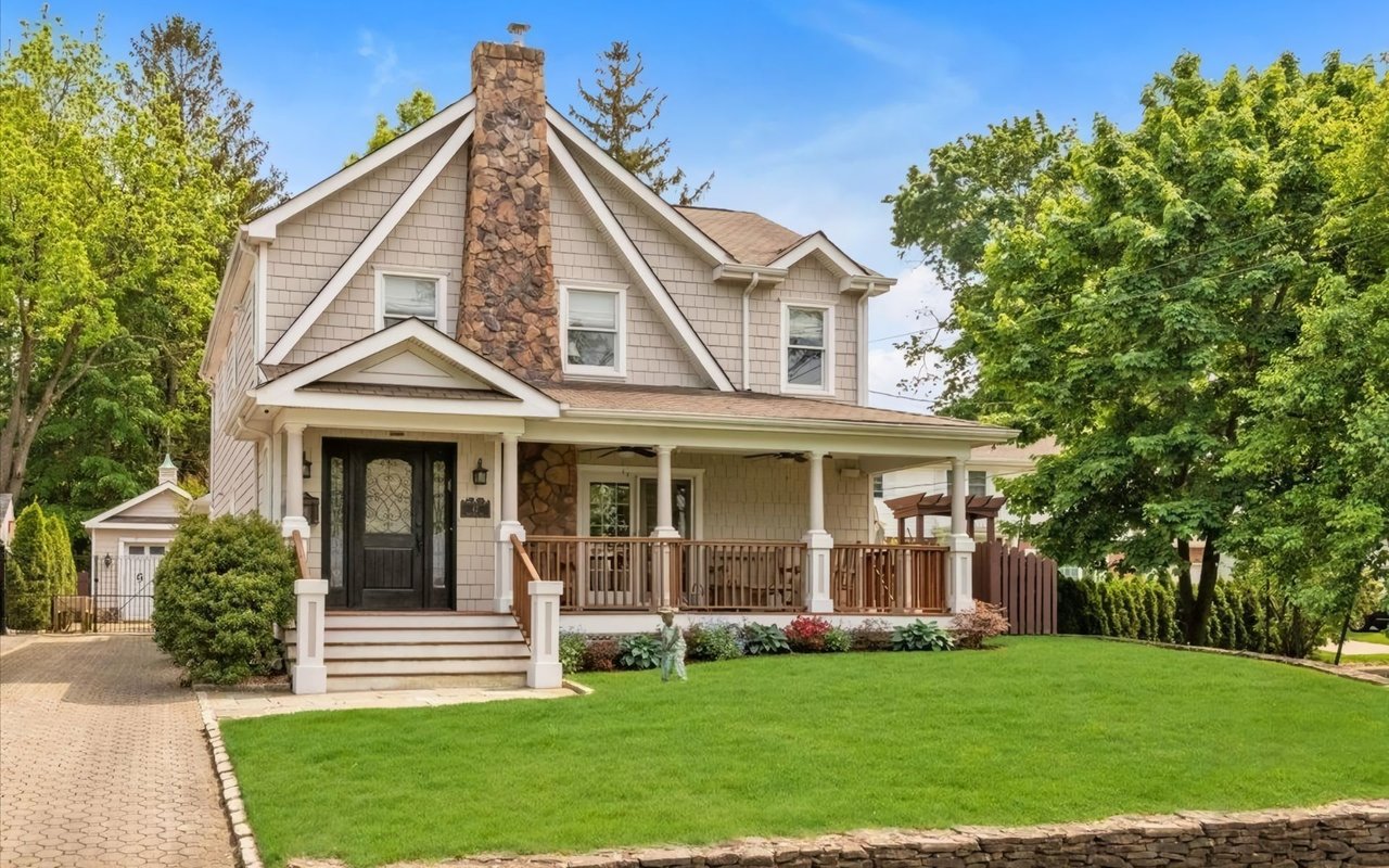 A two-story beige house with a stone chimney and a front porch.