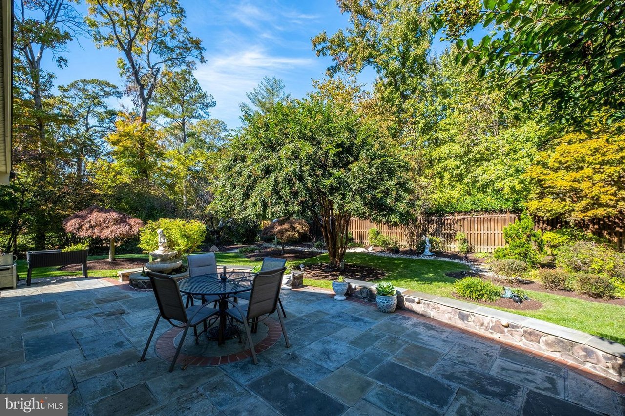 Stone patio with dining set overlooking a landscaped backyard with mature trees and a fountain.