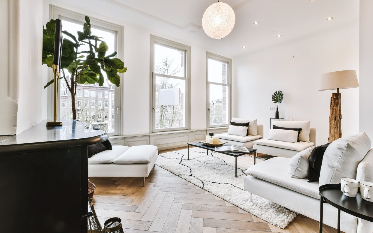 A living room with a cozy seating area, a coffee table, a tall lamp with a white shade, and large outdoor-view windows.