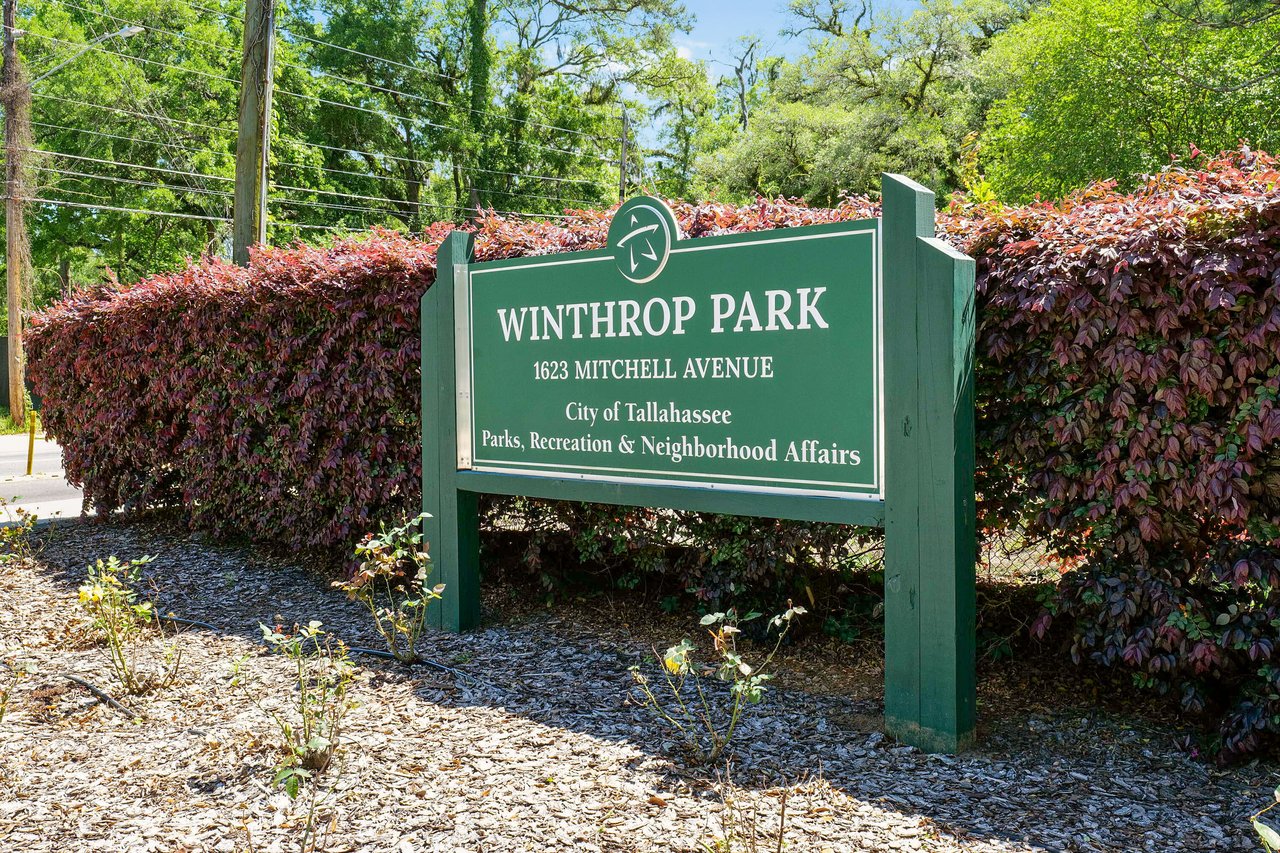 A ground-level view of a sign for "Winthrop Park" in the Betton Hills neighborhood, surrounded by lush greenery and flowers.