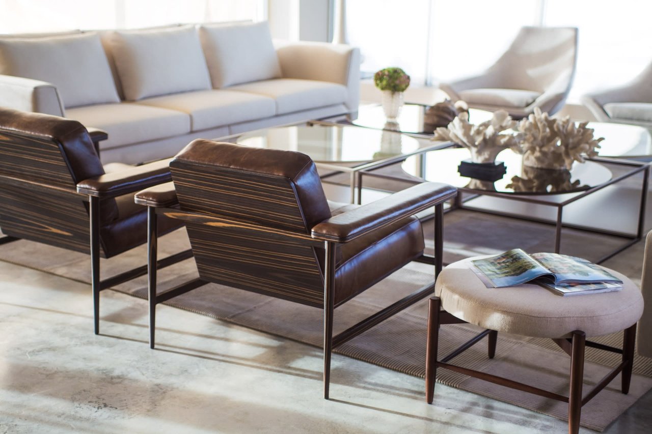 Bright living room with a pale sectional, dark leather armchairs, and glass coffee tables.