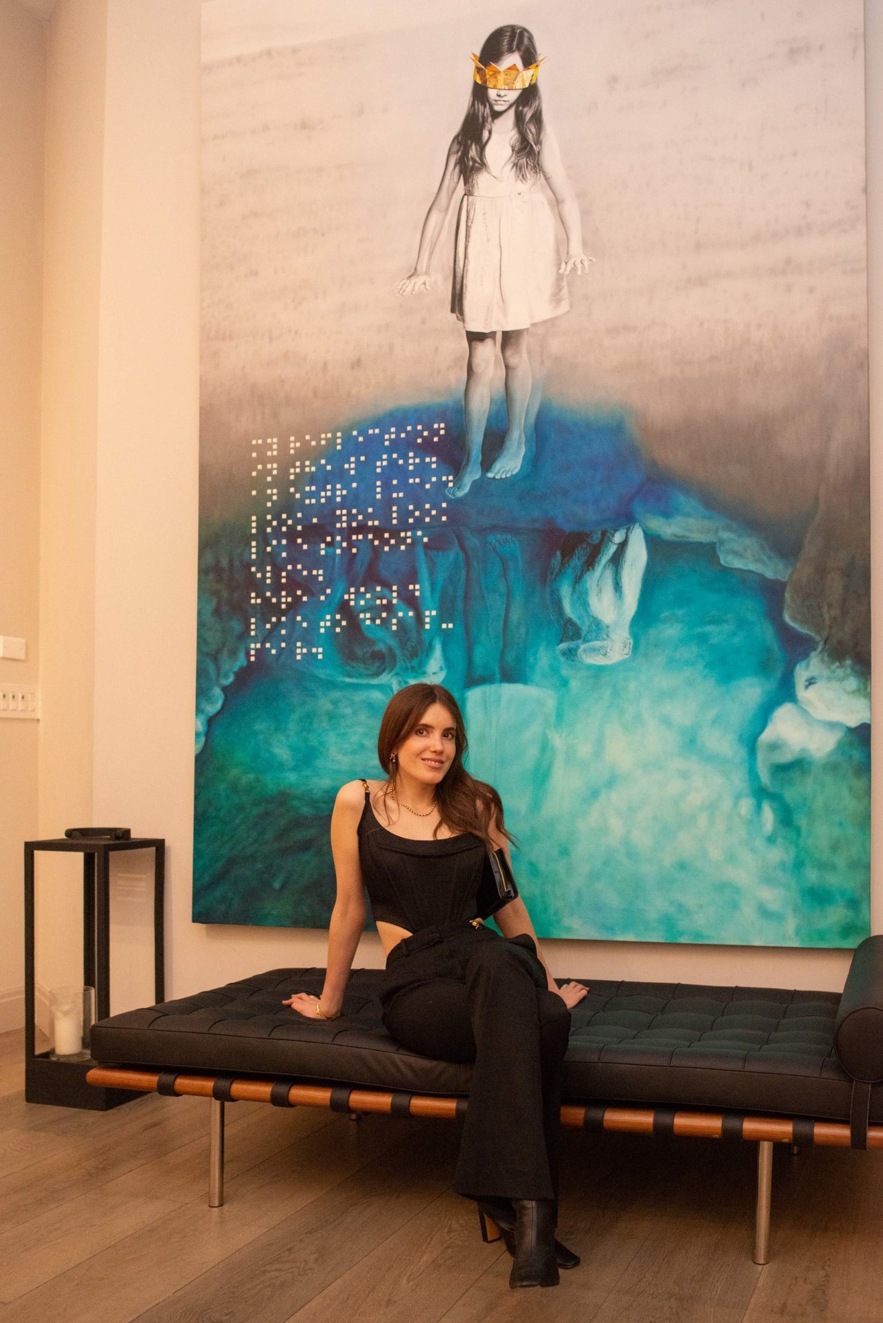 Woman seated on a dark bench in front of a large turquoise and peach artwork.