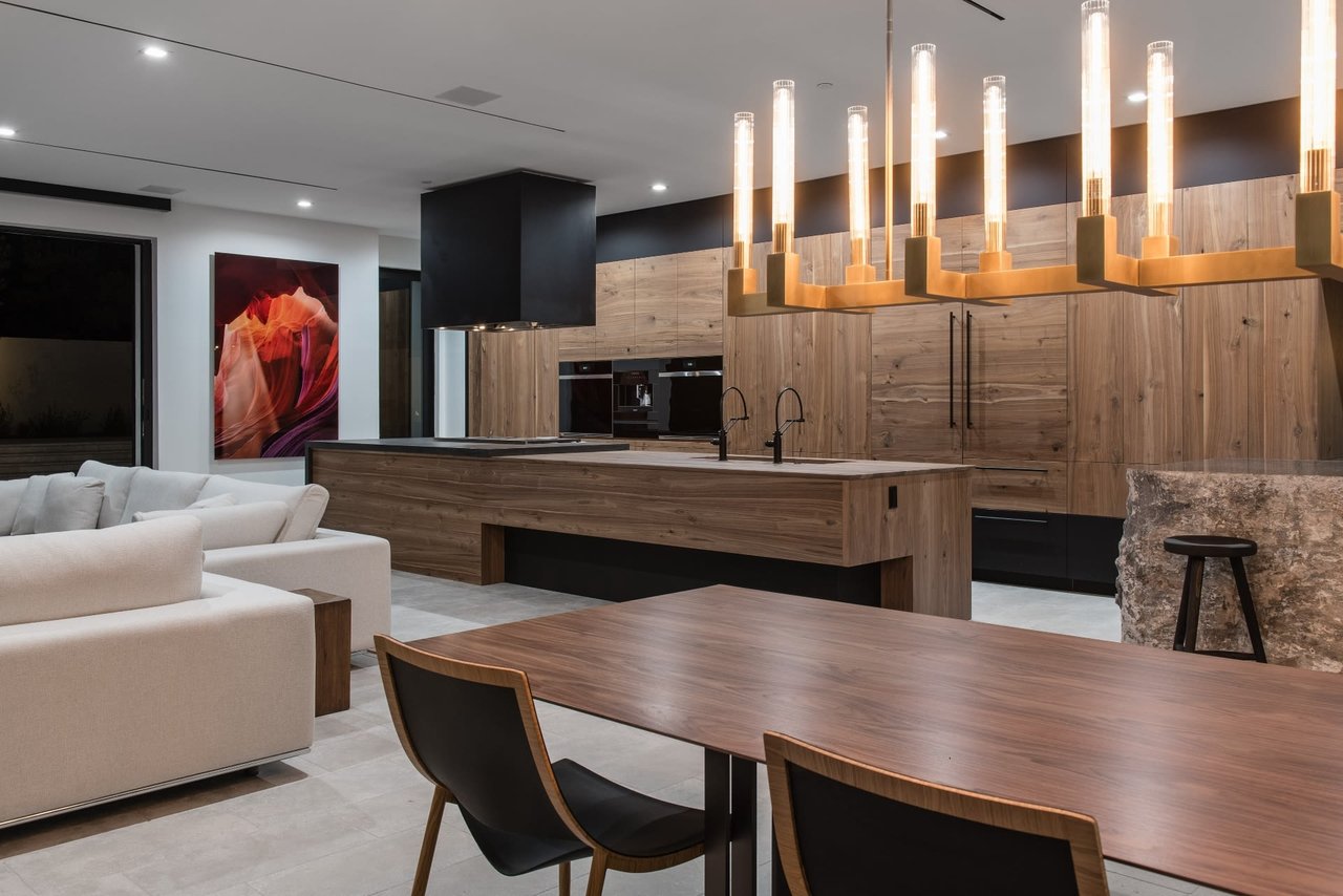 Modern kitchen with wood cabinetry, a large island, sculptural pendant lights, and an adjoining dining area.