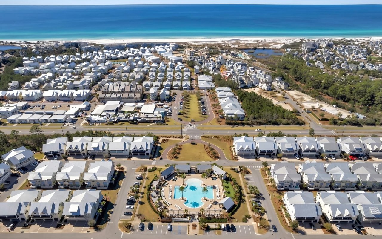 An aerial view of a coastal community with white houses, a pool, and a large parking lot.